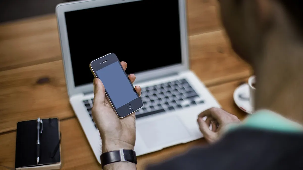 Homme assis devant un ordinateur portable, son téléphone à la main
