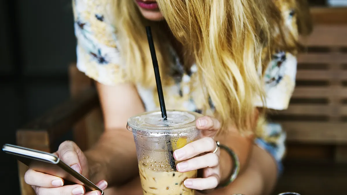 Jeune femme qui écrit un message sur son téléphone, un café glacé devant elle