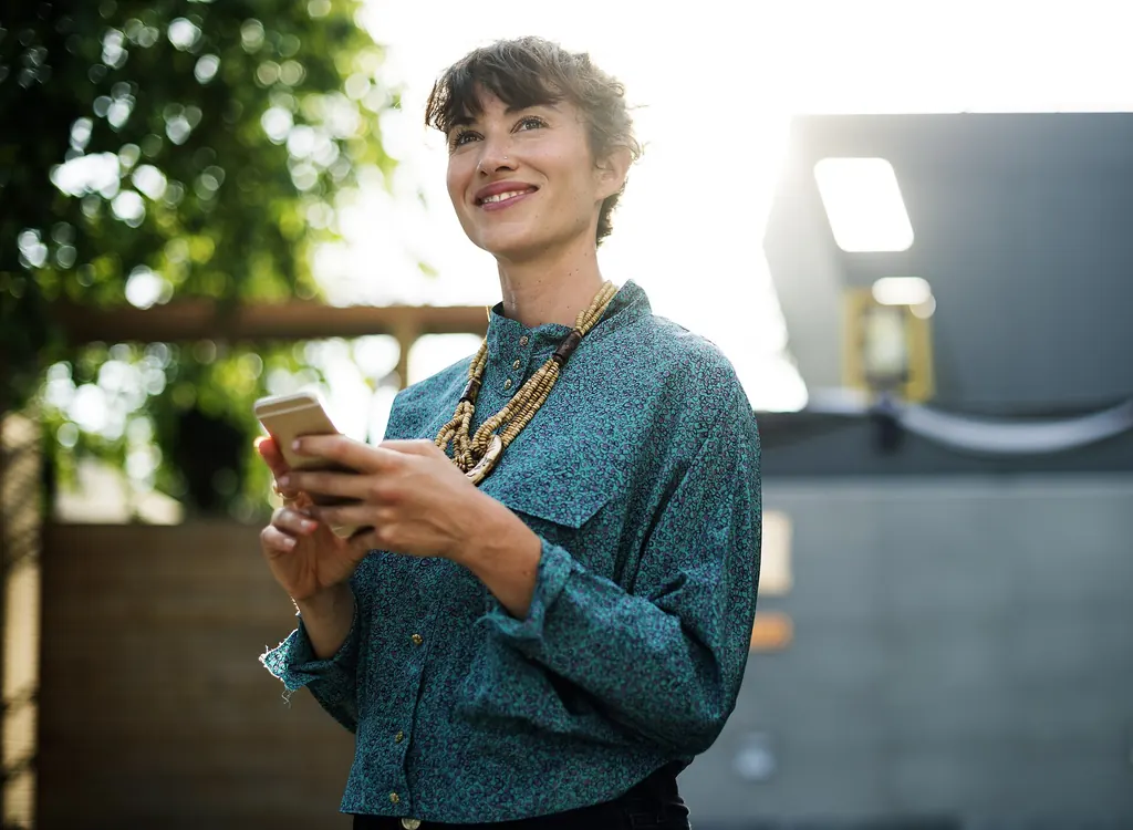 Femme souriante, téléphone en main, dans une rue ensoleillée