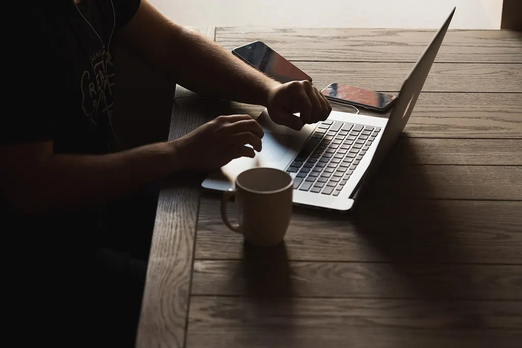 Mains sur le clavier d'un ordinateur portable, avec un téléphone et un café à côté