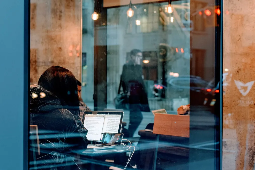 Femme devant son ordinateur portable, aperçue à travers la vitrine d'un café