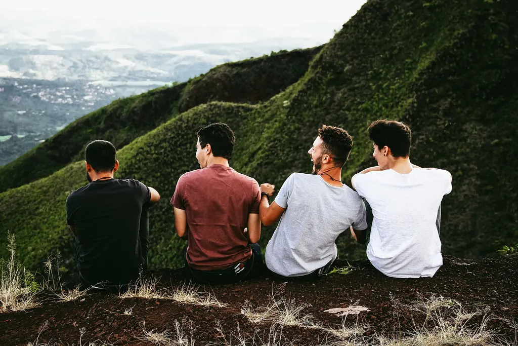 Quatre amis assis dans l'herbe au sommet d'une colline, face à la vallée