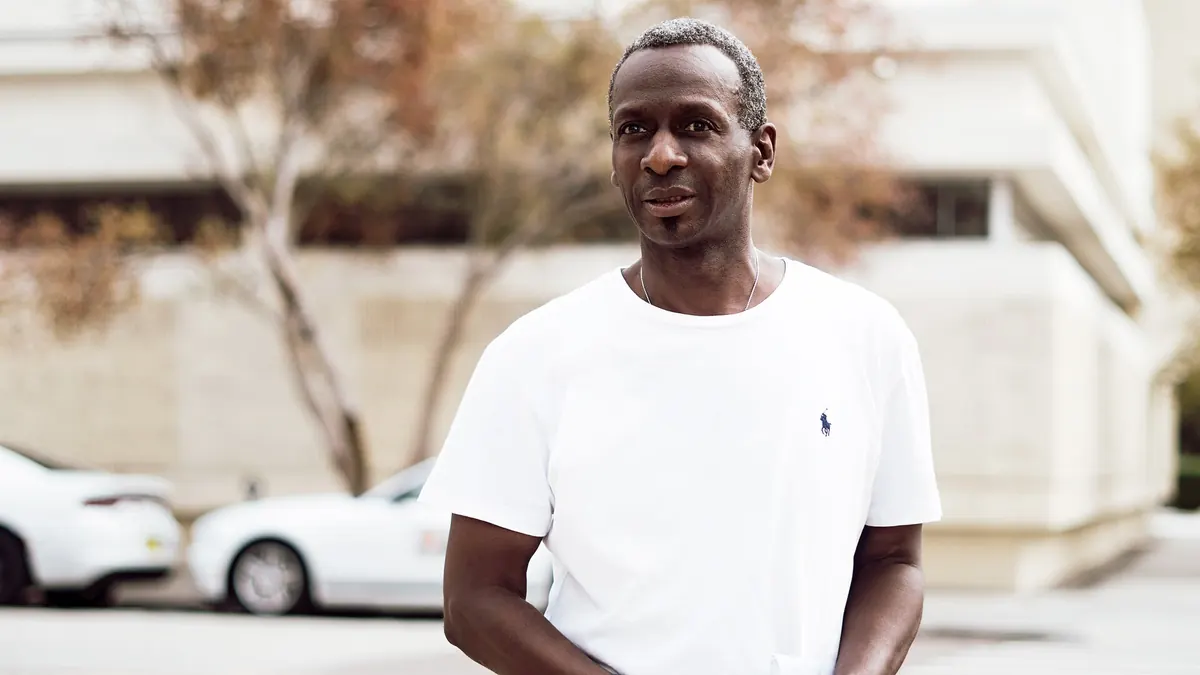 Homme souriant, épaules détendues et posture ouverte, debout dans une rue
