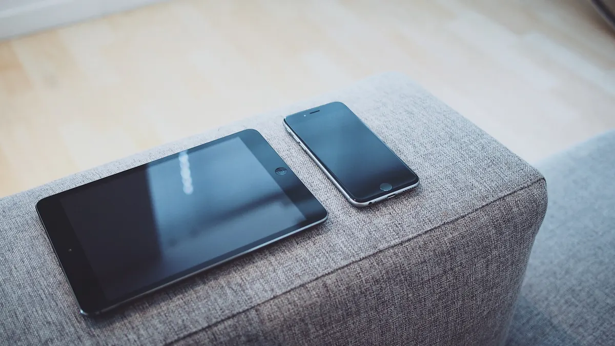 Téléphone et tablette éteints, posés côte à côte sur l'accoudoir d'un canapé