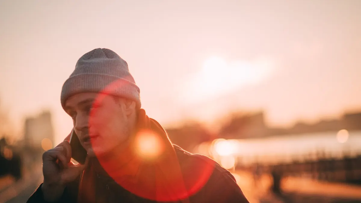 Jeune homme en bonnet qui téléphone dehors, au coucher du soleil