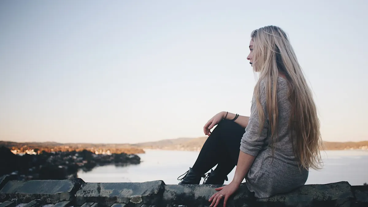 Jeune femme assise sur un ponton, le regard tourné vers le lac