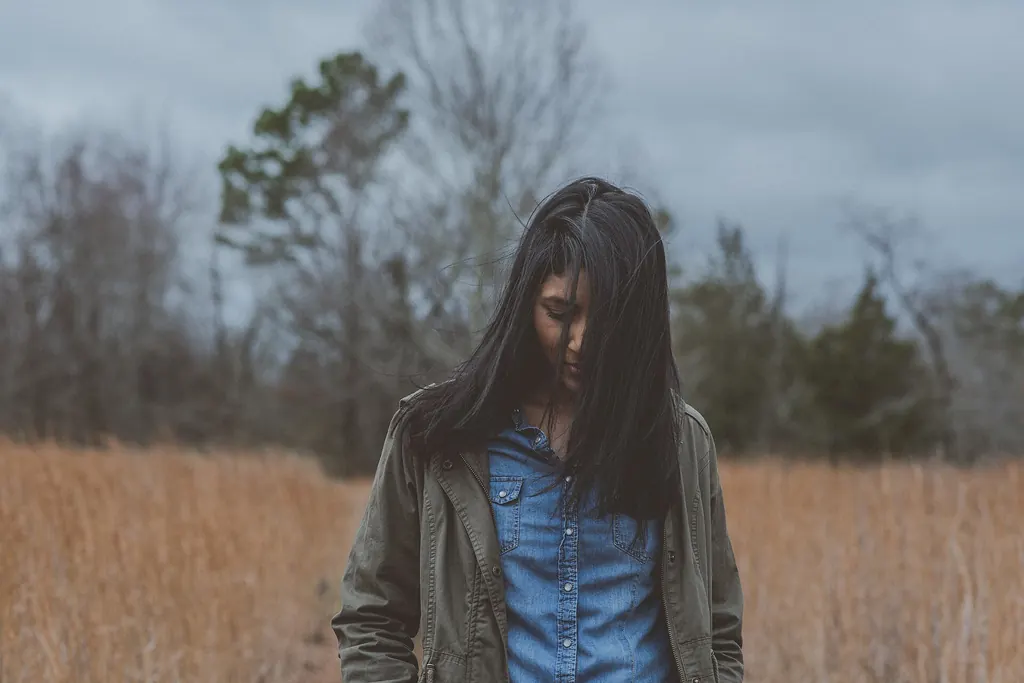 Jeune femme pensive, le regard baissé, au milieu d'un champ