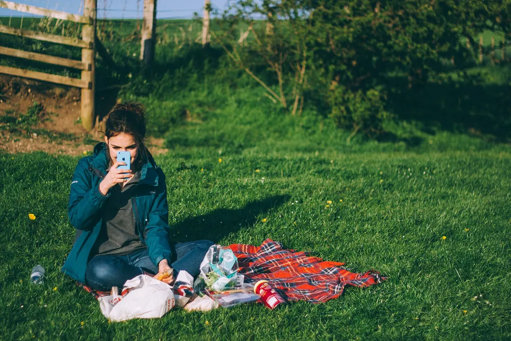 Jeune femme assise seule dans l'herbe, son téléphone levé devant elle